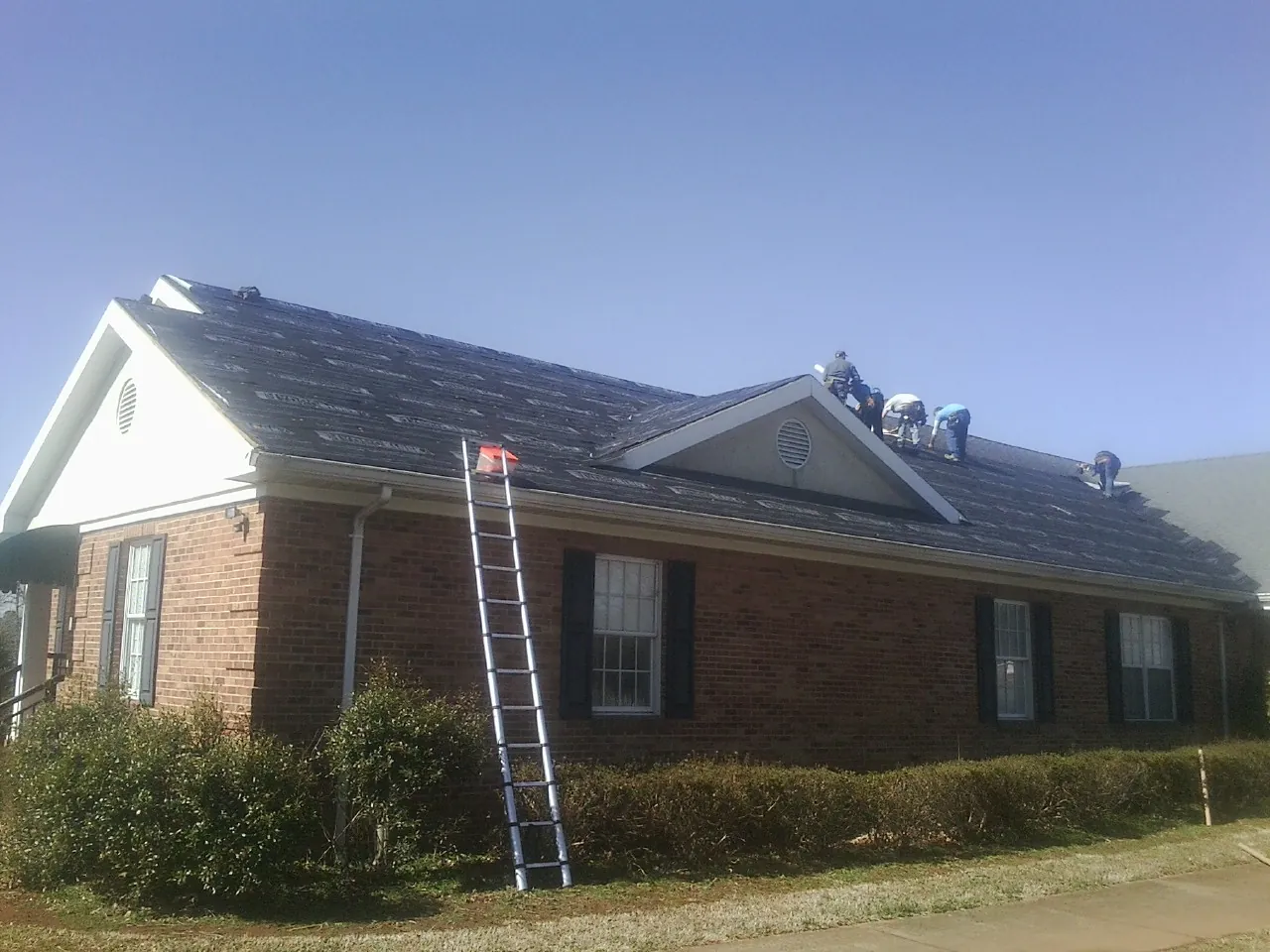 Crew tearing shingles off a brick ranch roof with a ladder set — Metal Roof Repair work by our crew in Surprise