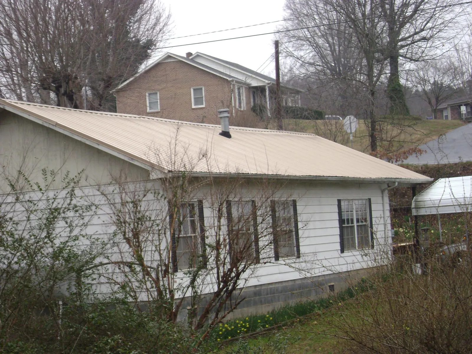Tan metal roof on a white sided house set into a hillside — Commercial Roofing by Roofing Brothers in Surprise